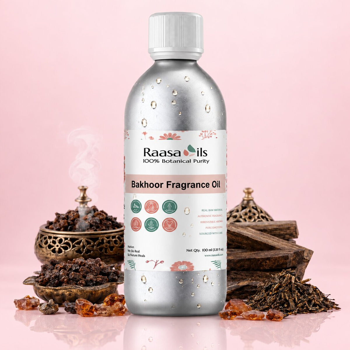 A bottle of Raasa oils Bakhoor Fragrance Oil centered on a pink background, surrounded by decorative incense, wood pieces, and amber resin pieces. The bottle is metallic silver with a white cap and a white label featuring pink and green botanical illustrations.
