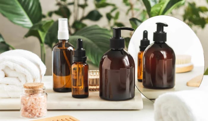 Brown glass bottles and jars on a marble surface with a mirror and towels in the background.