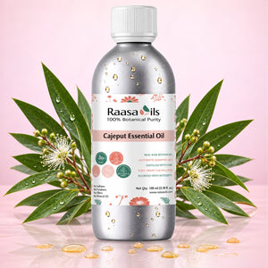A bottle of Raasa oils Cajapeut Essential Oil centered against a soft pink background, flanked by green leaves and small white flowers with water droplets. The bottle is metallic silver with a white cap and a white label featuring pink and green botanical illustrations.