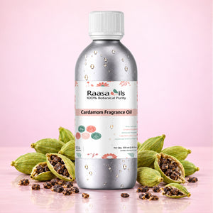 A bottle of Raasails Cardamom Fragrance Oil centered on a pink background, surrounded by whole and halved green cardamom pods with dark seeds. The bottle is metallic silver with a white cap and a white label featuring pink floral accents and product text.