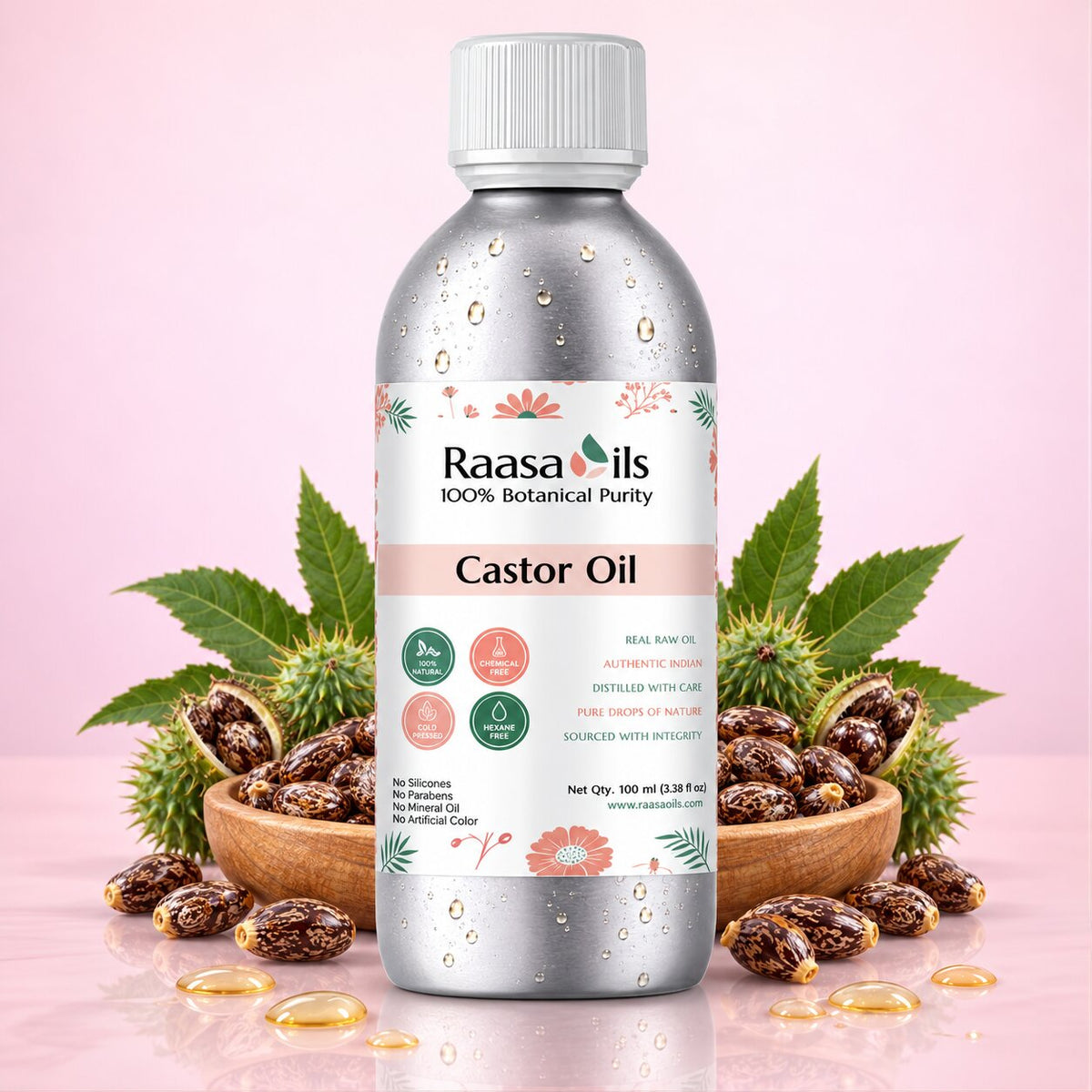 A bottle of Raasa oils Caster Oil centered on a soft pink background, styled with wooden bowls of castor seeds and scattered castor oil around its base.