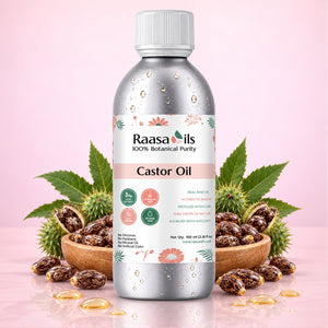 A bottle of Raasa oils Caster Oil centered on a soft pink background, styled with wooden bowls of castor seeds and scattered castor oil around its base.