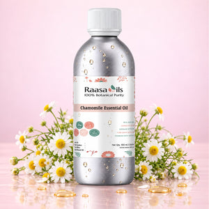A bottle of Raasa oils Chamomile Essential Oil centered on a pink background, flanked by chamomile flowers and gold oil droplets. The bottle is metallic silver with a white cap and a white label featuring the brand name 'Raasa oils'.