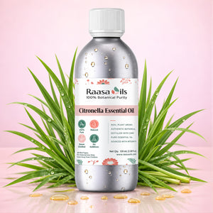 A bottle of Raasa Oils Citronella Essential Oil centered on a light pink background, surrounded by green citronella leaves with water droplets and scattered golden oil droplets. The bottle is metallic silver with a white cap and a white label featuring pink and green accents.