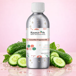 A bottle of Raasa Oils Cucumber Fragrance Oil centered on a pink background, surrounded by fresh cucumber slices, whole cucumbers, and green leaves. The bottle is metallic silver with a white cap and a white label featuring pink and green accents.