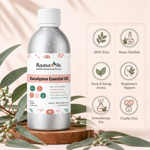 A bottle of Raasa oils Eucalyptus Essential Oil displayed on a wooden stand with eucalyptus leaves. The bottle is metallic silver with a white cap and a white label featuring pink floral accents and green icons.