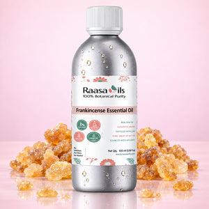 A bottle of Raasa Oils Frankincense Essential Oil centered on a pink background, surrounded by clusters of amber-colored frankincense resin. The bottle is metallic silver with a white cap and a white label featuring green and pink details.