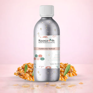 Raasa Oils Frankincense Essential Oil bottle with frankincense resin and leaves on a pink background