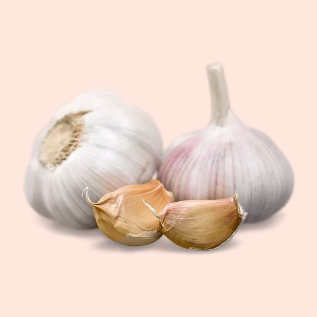 Two whole garlic bulbs and one split garlic on a light pink background
