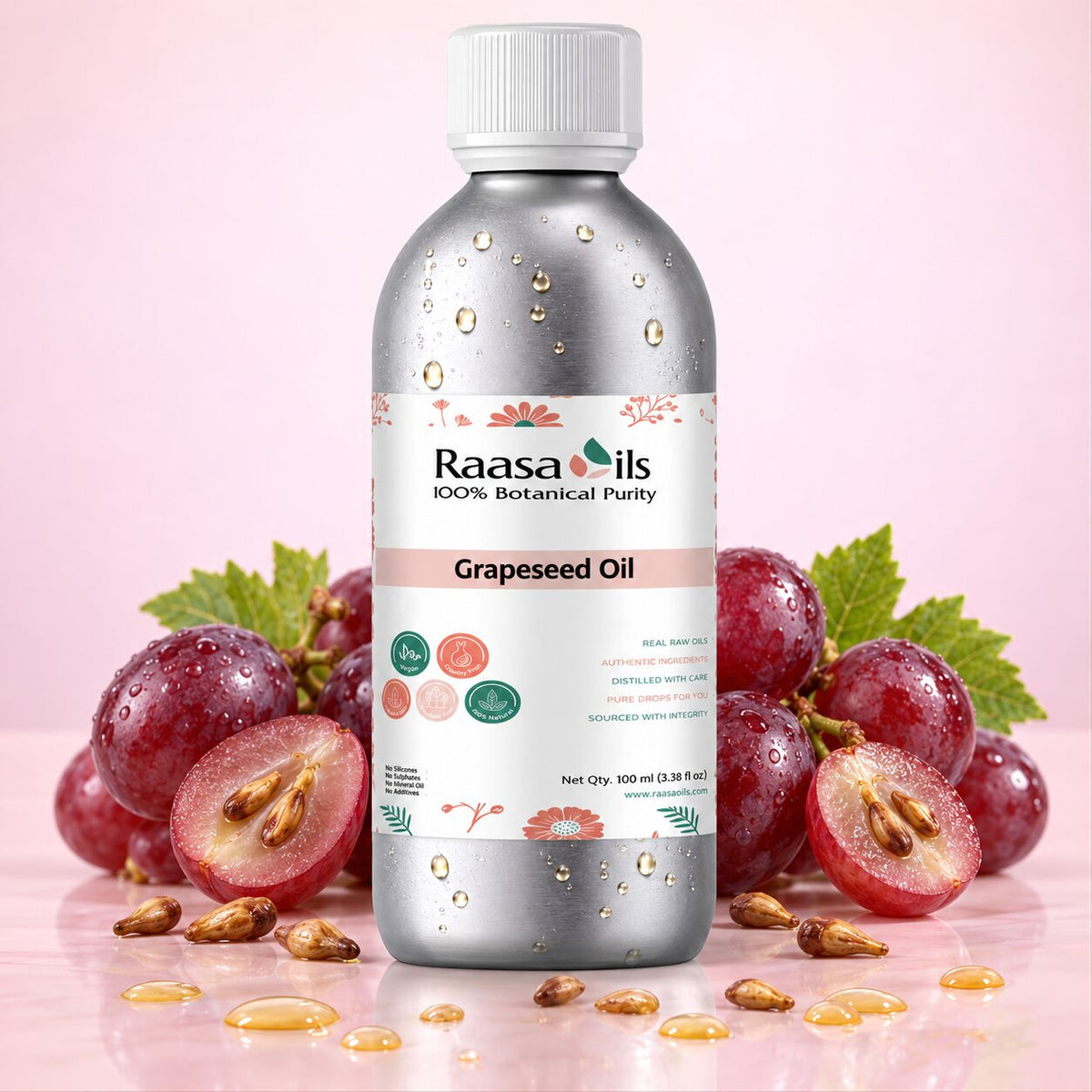 A bottle of Raasa oils Grapeseed Oil centered on a pink background, flanked by fresh red grapes, sliced grapes, and scattered oil droplets. The bottle is metallic silver with a white cap and a white label featuring pink and green accents.