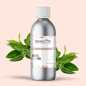 Silver bottle of Raasa Oils Green Tea Essential Oil with tea leaves on a light pink background