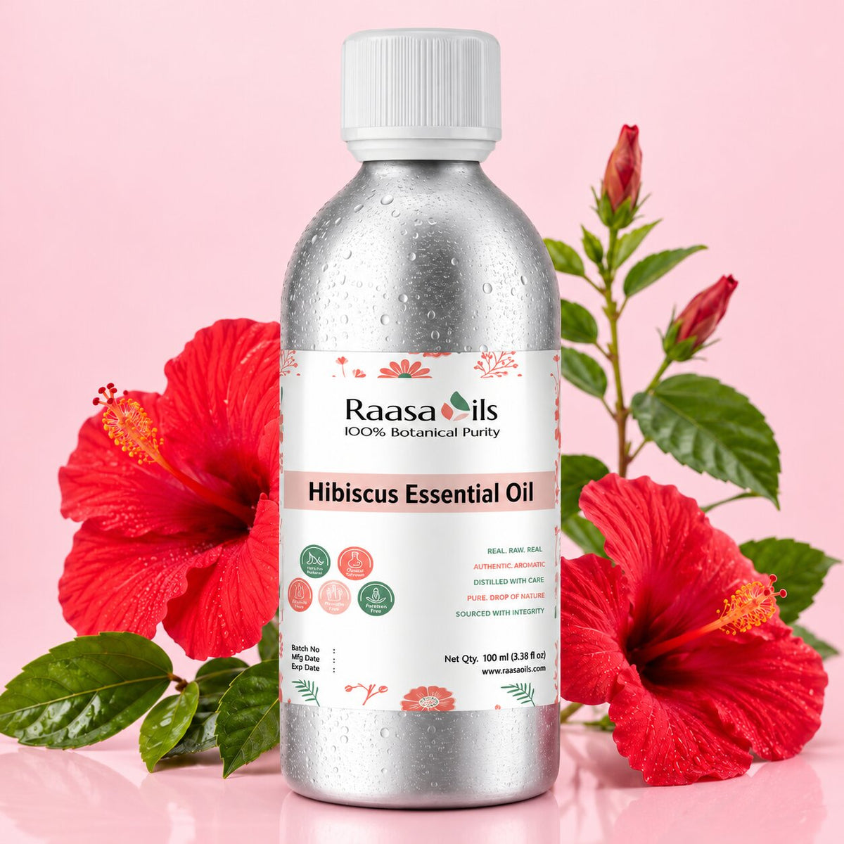 A bottle of Raasa Oils Hibiscus Essential Oil centered on a pink background, flanked by red hibiscus flowers and green leaves. The bottle is metallic silver with a white cap and a white label featuring pink and green text and graphics.