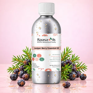 A bottle of Raasa Oils Juniper Berry Essential Oil centered on a soft pink background, surrounded by green juniper sprigs, two dark blue-black berries, and scattered golden oil droplets.