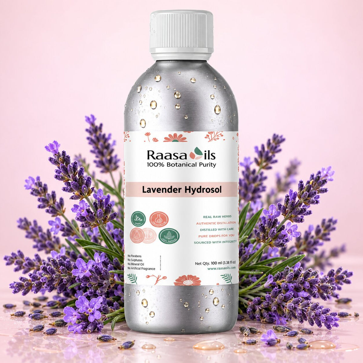 A bottle of Raasails Lavender Hydrosol centered on a pink background, surrounded by sprigs of purple lavender flowers. The bottle is metallic silver with a white cap and a white label featuring pink and green accents.
