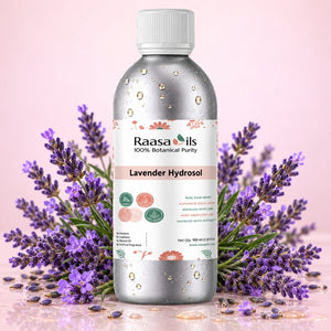 A bottle of Raasails Lavender Hydrosol centered on a pink background, surrounded by sprigs of purple lavender flowers. The bottle is metallic silver with a white cap and a white label featuring pink and green accents.