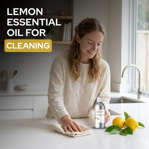 Woman cleaning a kitchen counter with lemon essential oil and lemons on a table.