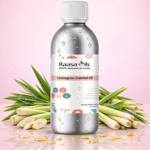 A bottle of Raasa oils Lemongrass Essential Oil centered on a pink background, flanked by fresh lemongrass stalks with scattered golden oil droplets on the bottle and surface.