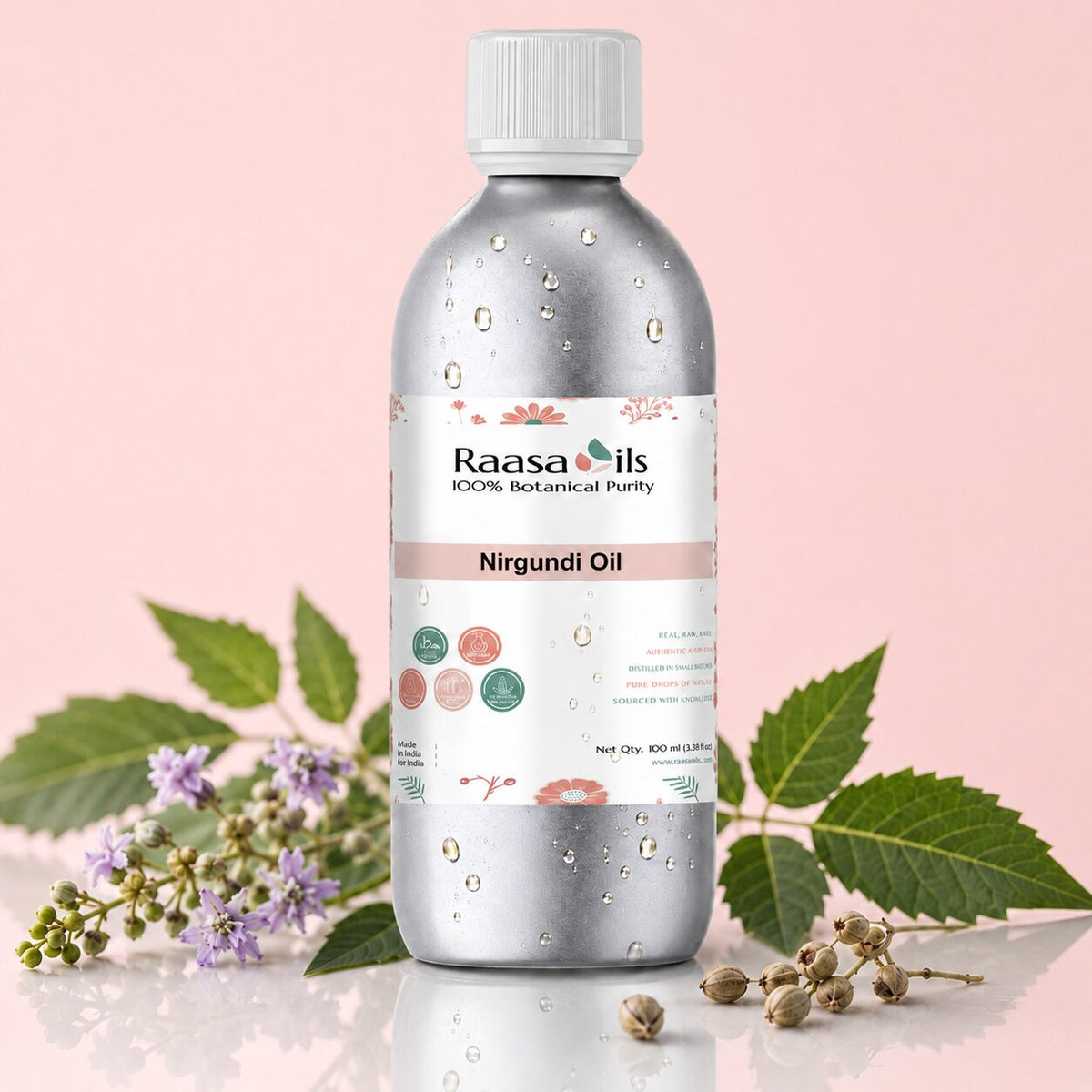 A bottle of Raasa oils Nirgundi Oil, 100 ml, with a silver metallic body, white cap, and a white label with botanical illustrations. The bottle is styled with green leaves and small purple flowers on a reflective surface against a soft pink background.