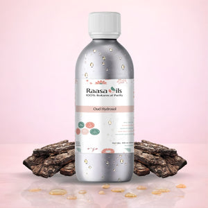Bottle of Raasa Oils Oud Hydrosol with dried oud wood on a pink background