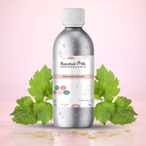 Bottle of Raasa Oils Patchouli Hydrosol with green leaves on a pink background