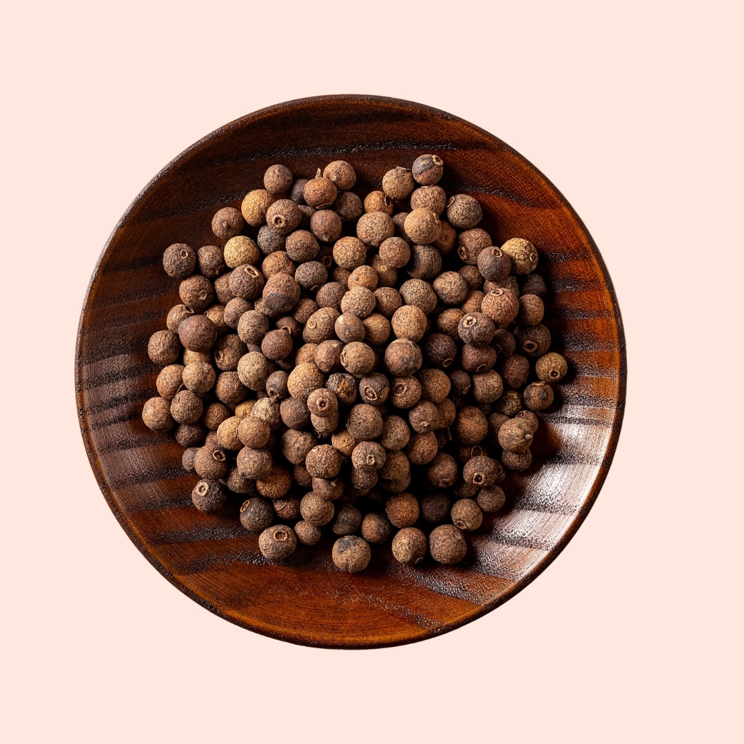 Wooden bowl filled with whole spices on a pink background