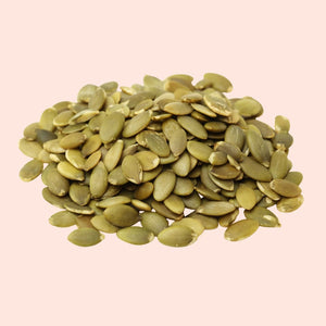Pile of green pumpkin seeds on a light pink background