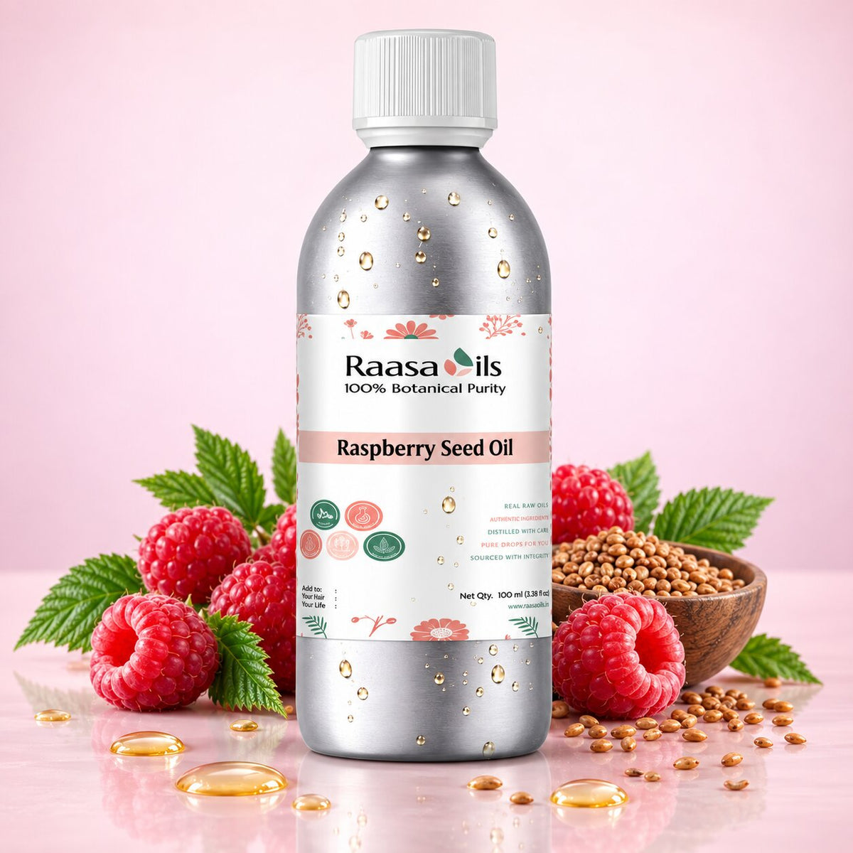A bottle of Raasa Oils Raspberry Seed Oil centered on a pink background, surrounded by fresh raspberries, green leaves, a small bowl of seeds, and scattered golden oil droplets. The bottle is metallic silver with a white cap and a white label featuring pink and green accents.