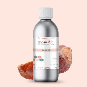 Bottle of Raasa Oils Reetha Oil with a shell and flowers on a light pink background