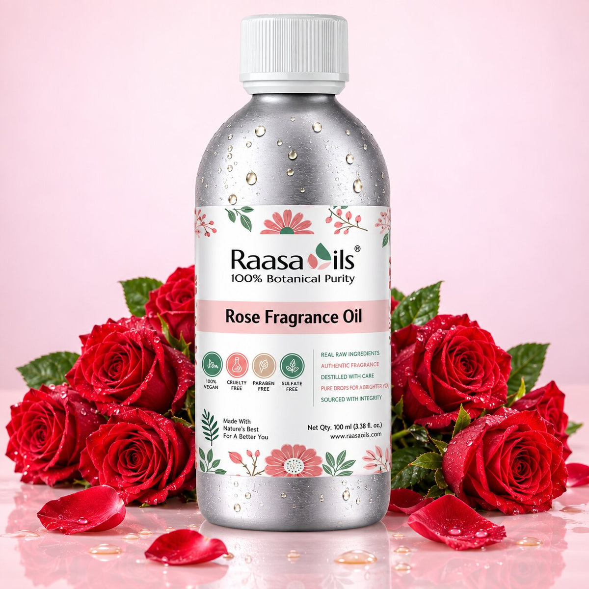 A bottle of Raasails Rose Fragrance Oil centered on a pink background, surrounded by red roses and rose petals. The bottle is metallic silver with a white cap and a white label featuring pink and green floral details.