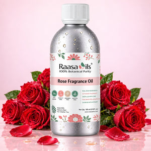 A bottle of Raasails Rose Fragrance Oil centered on a pink background, surrounded by red roses and rose petals. The bottle is metallic silver with a white cap and a white label featuring pink and green floral details.