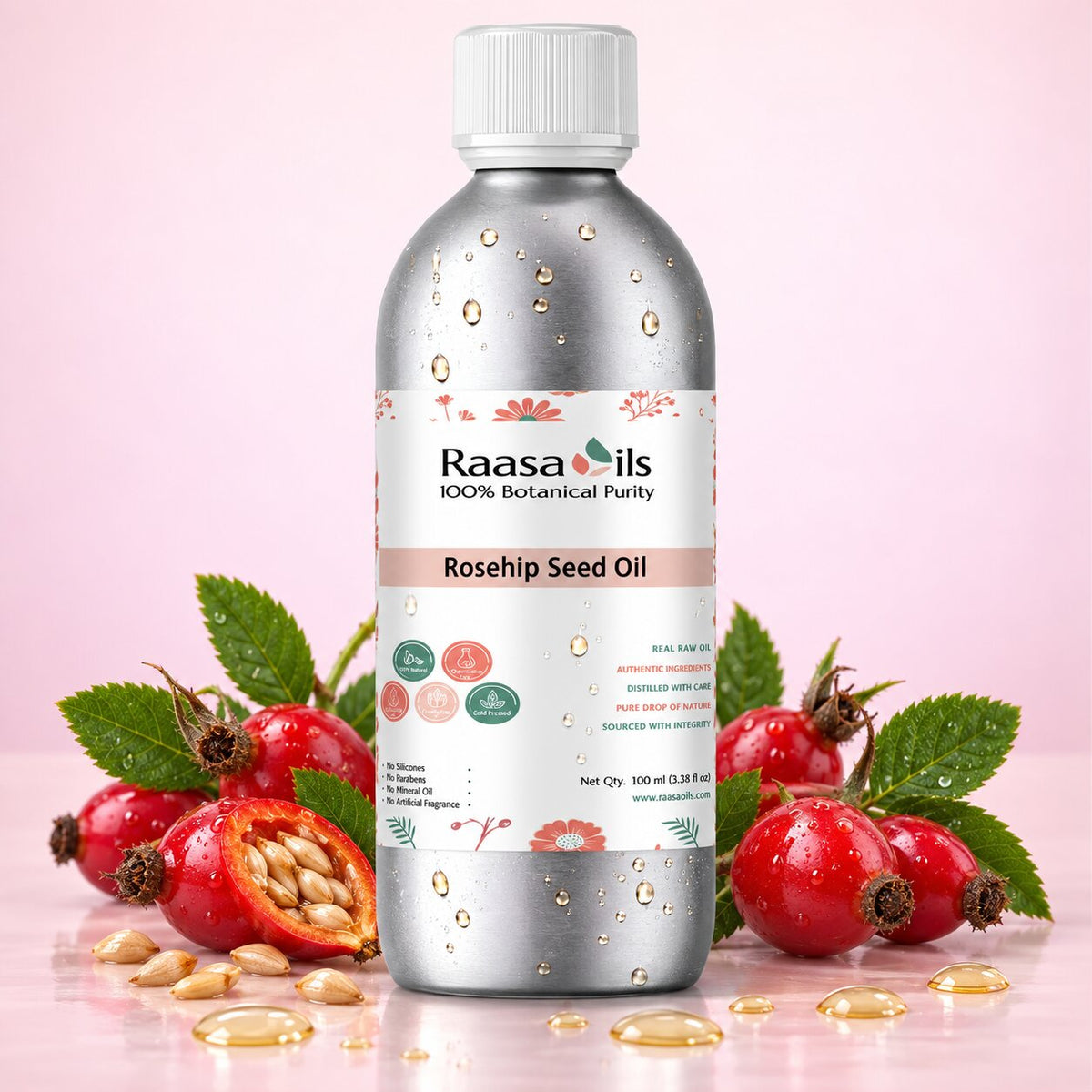 A bottle of Raasa Oils Rosehip Seed Oil centered on a pink background, surrounded by whole and halved red rosehips, green leaves, and scattered golden oil droplets. The bottle is metallic silver with a white cap and a white label featuring pink and green accents.