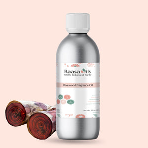 Bottle of Raasa Oils Rosewood Fragrance Oil with rosewood logs on a light pink background