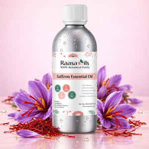 A bottle of Raasa Oils Saffron Essential Oil centered on a pink reflective surface, surrounded by purple saffron flowers and red saffron threads. The bottle is metallic silver with a white cap and a white label featuring pink and green accents.