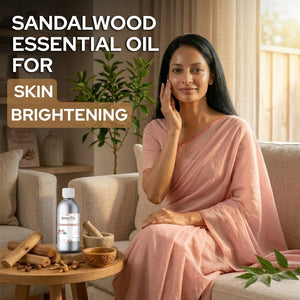 Woman in a pink saree sitting on a couch with sandalwood essential oil bottle and leaves on a table.