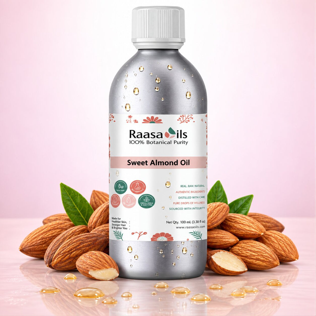 A bottle of Raasa Oils Sweet Almond Oil centered on a pink gradient background, surrounded by whole and sliced almonds with green leaves and scattered oil droplets. The bottle is metallic silver with a white cap and a white label featuring pink and green accents.