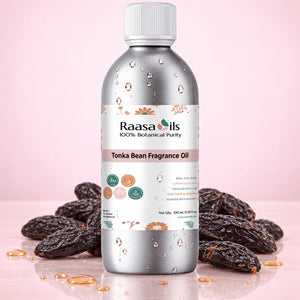 A bottle of Raasa Oils Tonka Bean Fragrance Oil stands upright on a reflective surface, surrounded by dark brown tonka beans and small droplets of golden oil, against a soft pink background.
