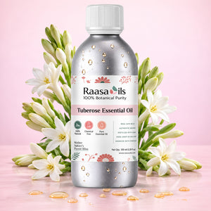 A bottle of Raasa oils Tuberose Essential Oil centered on a pink background, surrounded by white tuberose flowers and scattered golden oil droplets. The bottle is metallic silver with a white cap and a white label featuring pink and green accents.