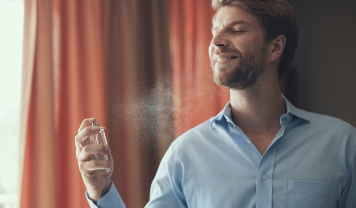 Man applying perfume in a room with red curtains