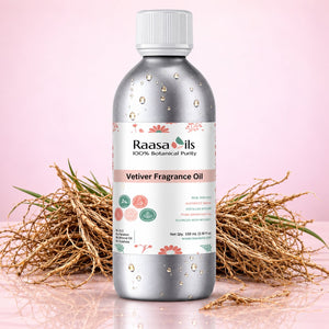 A bottle of Raasa oils Vetiver Fragrance Oil, 100 mL, with a silver metallic finish, white cap, and a white label with botanical illustrations, set against a pink background with dried vetiver grass props.