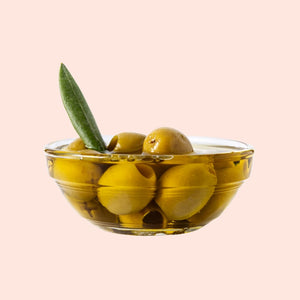Glass bowl with green olives on a light pink background