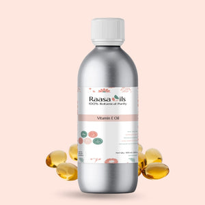 Bottle of Raasa Oils Vitamin E Oil with scattered capsules on a light pink background