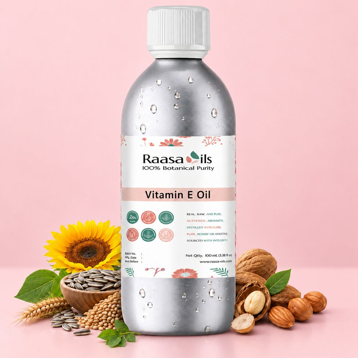 A bottle of Raasa oils Vitamin E Oil centered on a soft pink background, surrounded by natural ingredients including a sunflower, wheat, seeds, nuts, and mint leaves. The bottle is metallic silver with a white cap and a white label featuring pink and green accents.