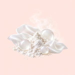 White cosmetic powder arranged in a small mound with three translucent glossy spheres and soft white fabric petals on a pale peach background.