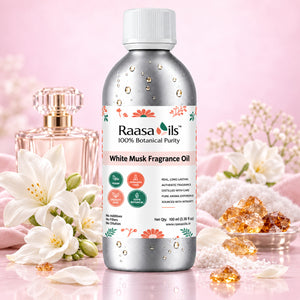 A bottle of Raasa oils White Musk Fragrance Oil stands centered on a reflective surface, surrounded by white flowers, crystals, and a perfume bottle against a soft pink background.