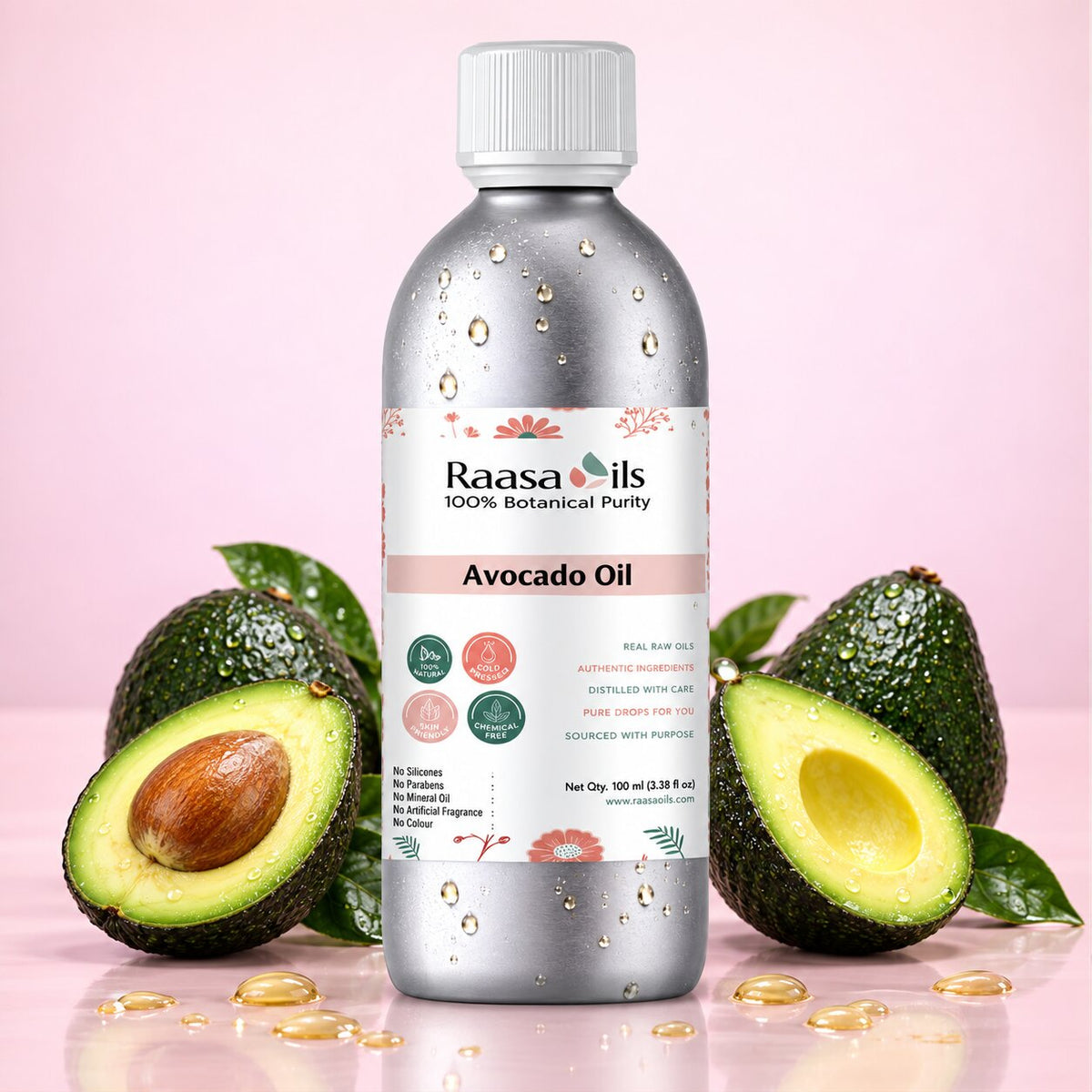 A bottle of Raasa Oils Avocado Oil centered on a pink background, flanked by whole and halved avocados with scattered golden oil droplets. The bottle is metallic silver with a white cap and a white label featuring pink floral accents and product details.