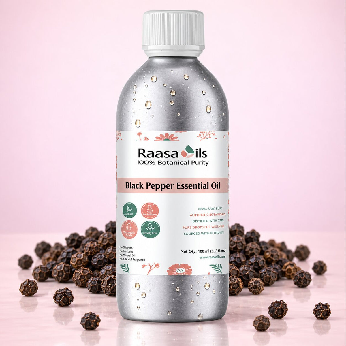 A bottle of Raasa oils Black Pepper Essential Oil centered on a light pink background, surrounded by scattered whole black peppercorns. The bottle is metallic silver with a white cap and a white label featuring pink and green accents.