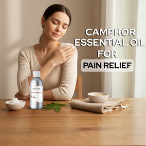 Woman holding a bottle of camphor essential oil with text about pain relief on a wooden table.