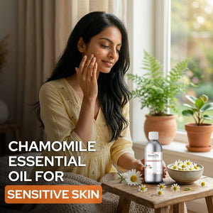 Woman applying chamomile essential oil to her skin with a bottle and flowers on a table.