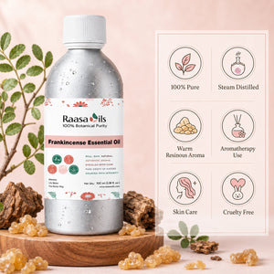 A bottle of Raasa Oils Frankincense Essential Oil stands on a wooden tray with dried roots and resin pieces around it. The bottle is metallic silver with a white cap and a white label featuring pink and green botanical illustrations.