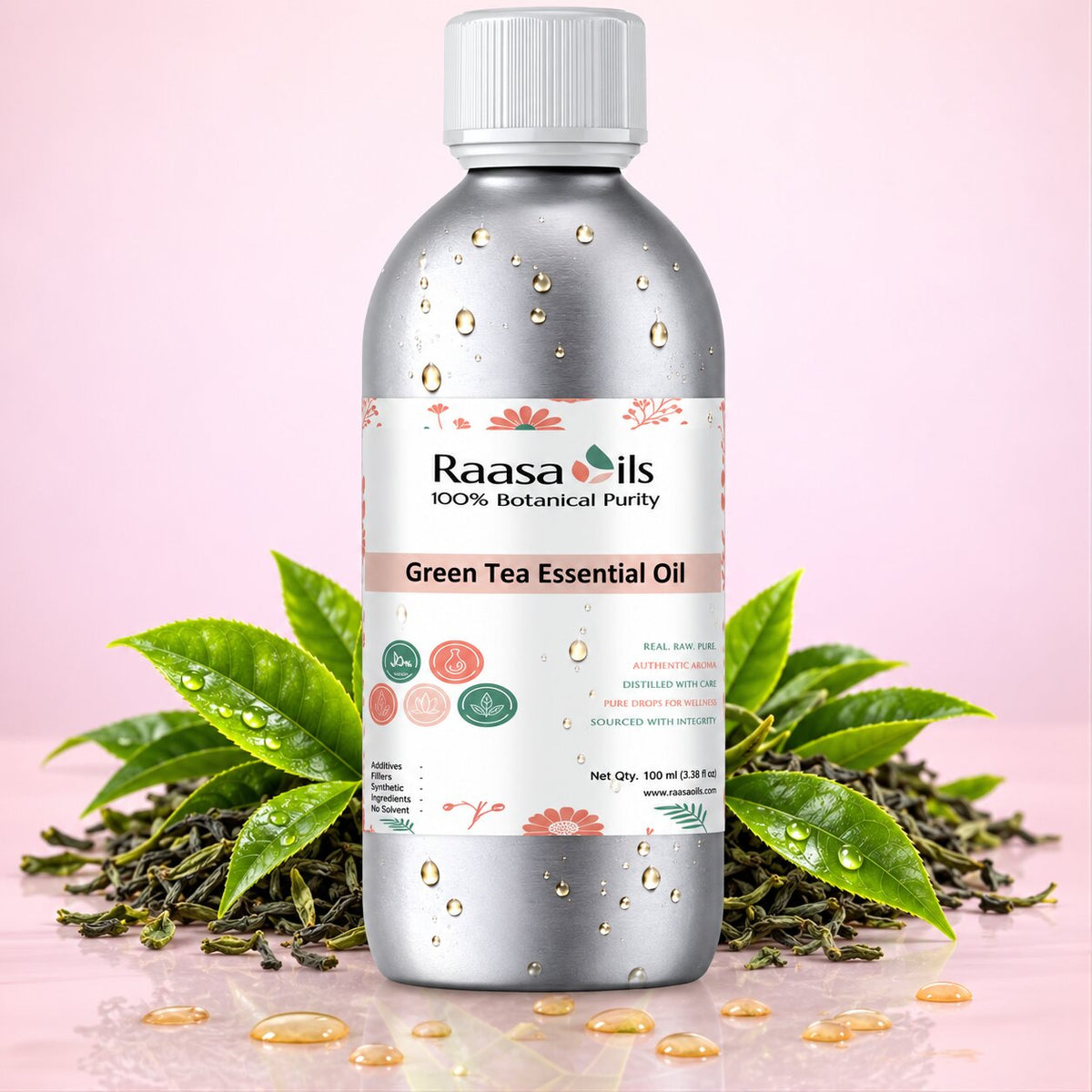 A bottle of Raasa Oils Green Tea Essential Oil centered on a pink background, surrounded by green tea leaves and loose tea buds with water droplets. The bottle is metallic silver with a white cap and a white label featuring green and pink accents.